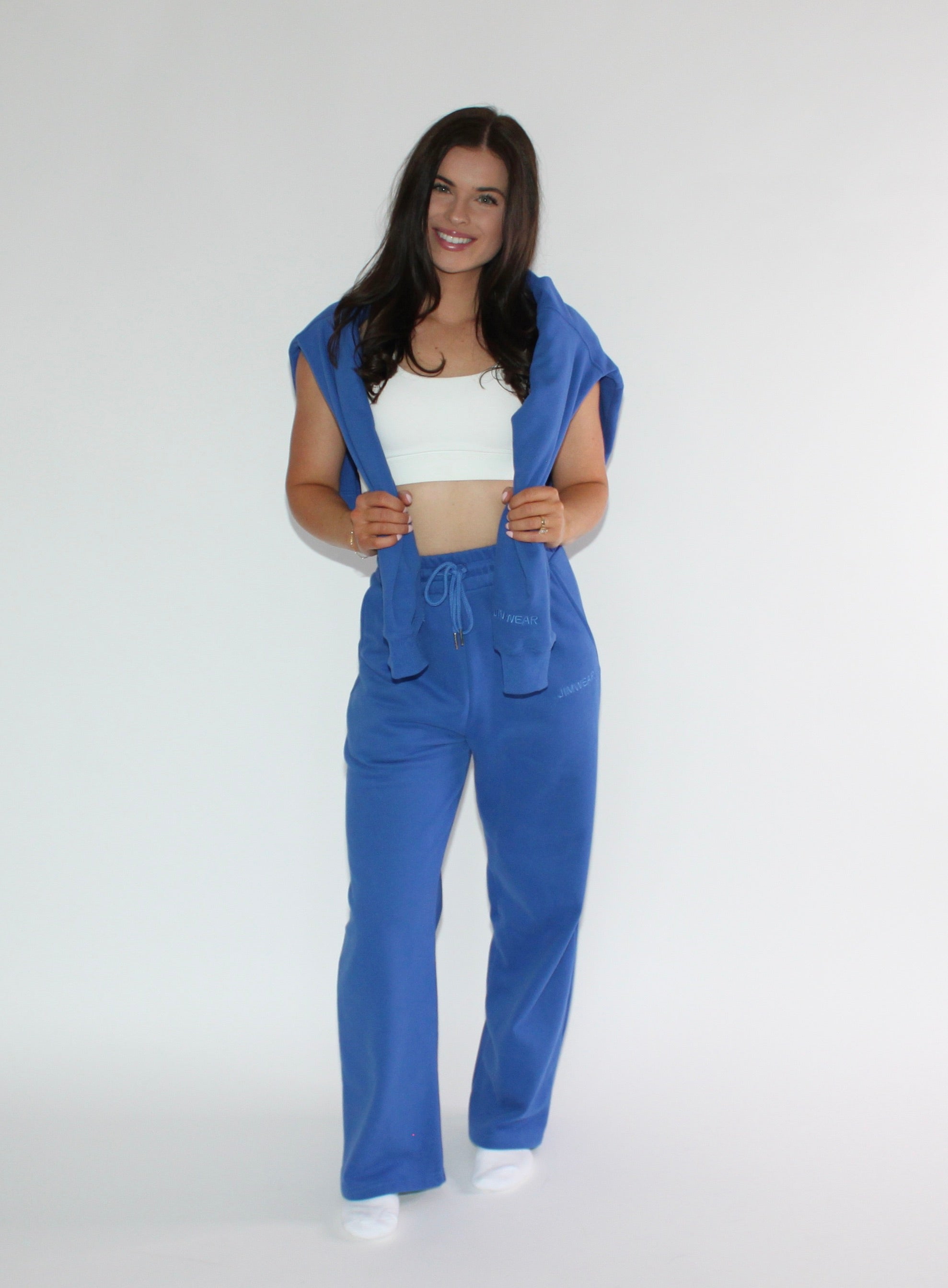 A woman modeling a matching royal blue lounge set consisting of a crewneck and wide-leg sweatpants, worn over a white sports bra against a light gray studio background.